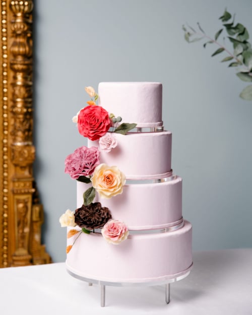 Fireetasjes rosa bryllupskake, pyntet med blomster.
