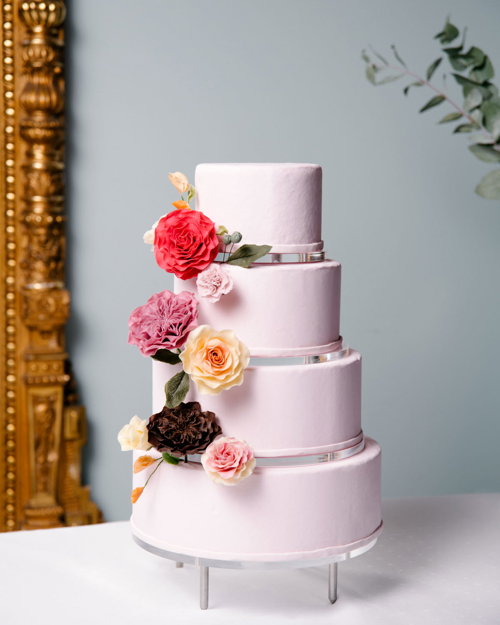 Fireetasjes rosa bryllupskake, pyntet med blomster.
