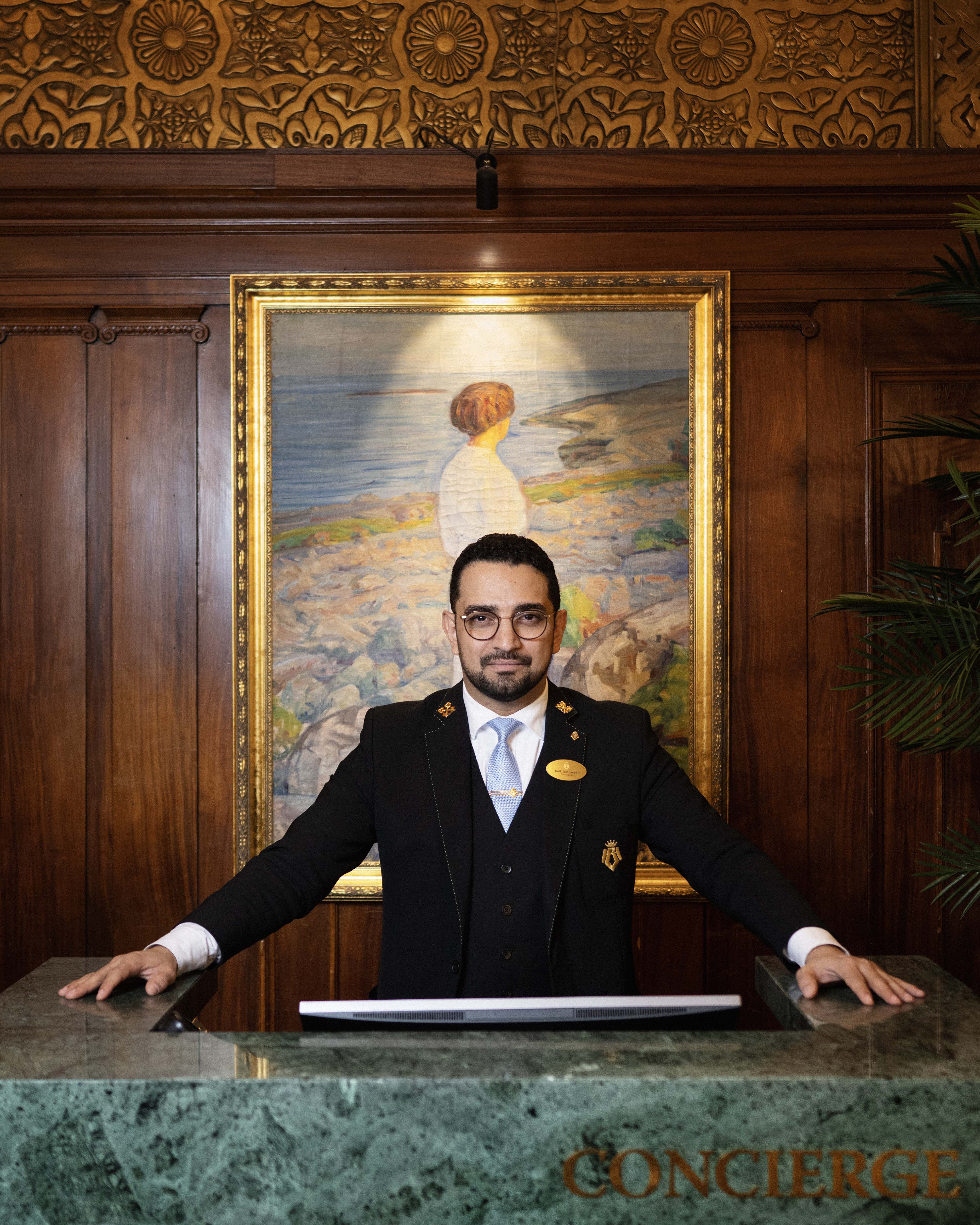 Portrett av smilende og glad concierge i uniform med turkis slips