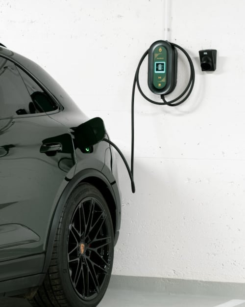 Back of a dark car parked in a garage with two charging cables on a white wall.