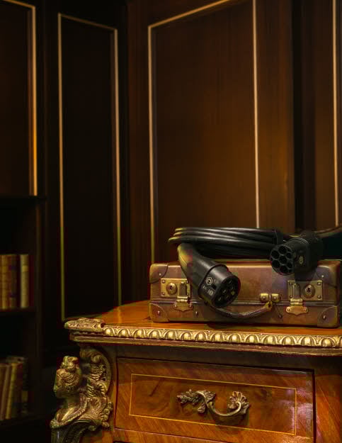 An electric car charging cable lying on top of a suitcase on a table in a room with dimmed lighting.
