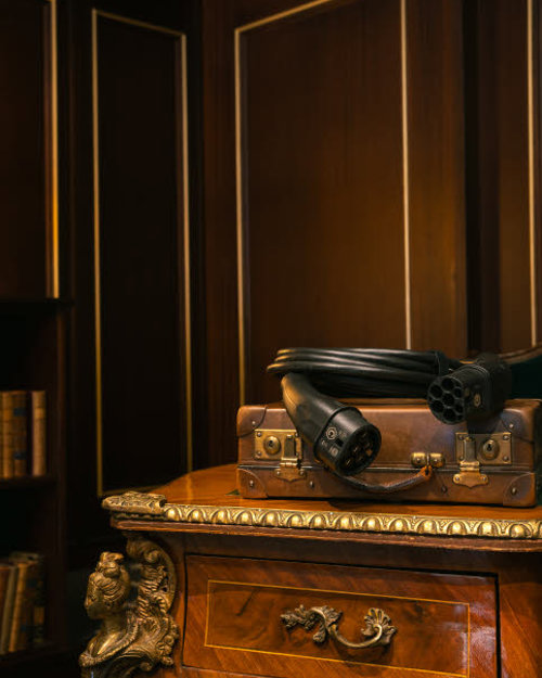 An electric car charging cable lying on top of a suitcase on a table in a room with dimmed lighting.