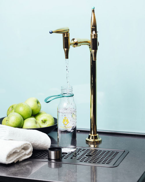 Grønne epler i en skål, hvite håndklær og en vannstasjon som fyller opp vannflaske med iskaldt vann