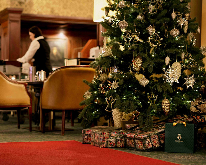 Pakker under juletre. Servitør arbeider i bakgrunnen.