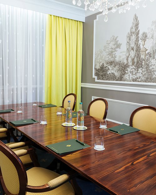 Møteromsbord i oljet treverk og stoler med grå vegger og gule gardiner