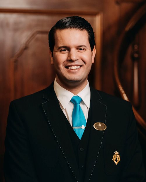 Et portrett av en smilende og glad concierge iført uniform og turkist slips