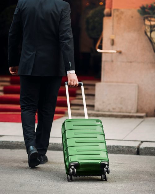 Mann triller grønn kabinkoffert inn mot inngangen til Hotel Bristol