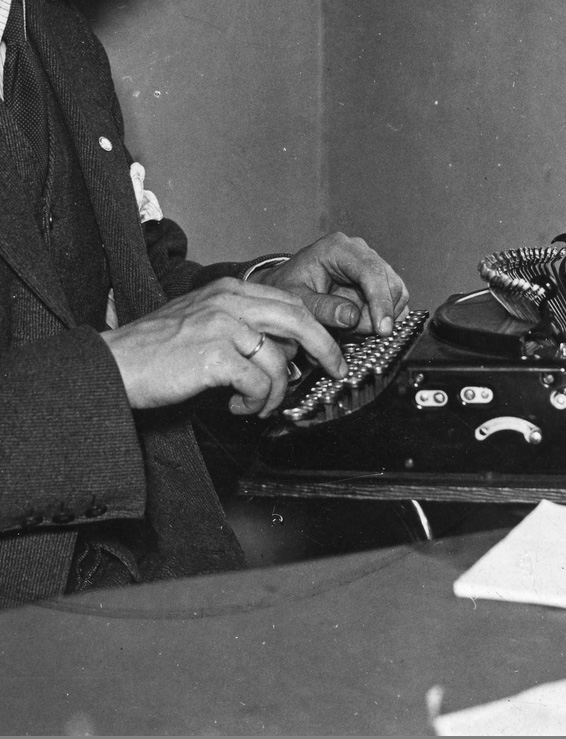 Svart-hvitt nærbilde av en hendene til en mann som skriver på en gammeldags skrivemaskin