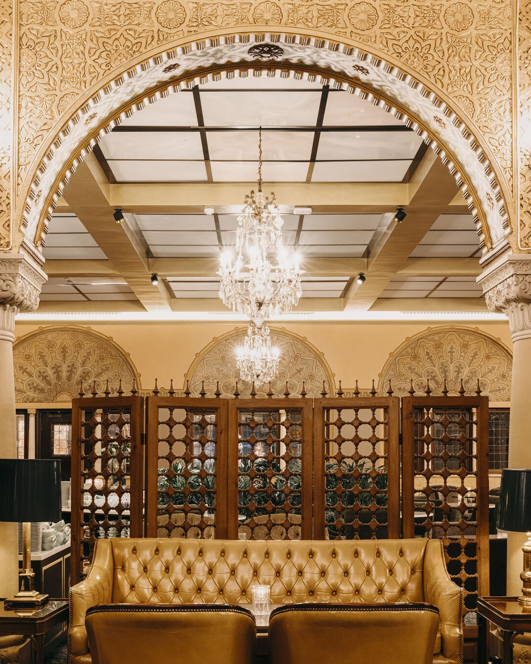 Symmetrisk bilde av Vinterhaven og Bibliotekbaren med sennepsgul skinnsofa og en stor lysekrone i bakgrunnen