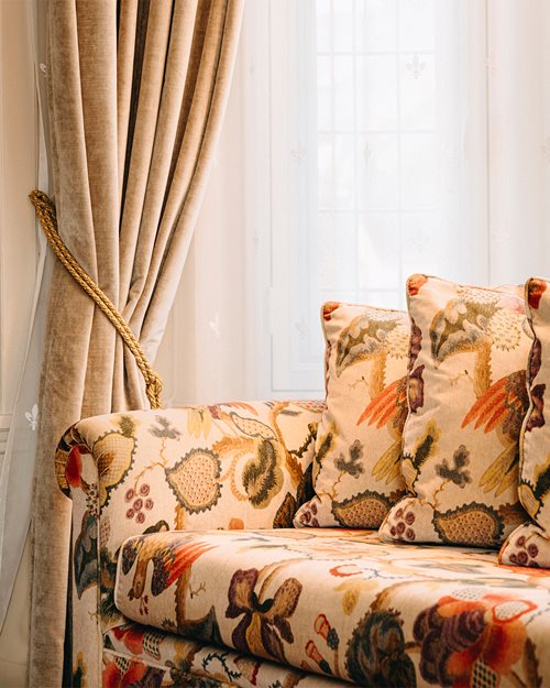 Mønstret sofa som står foran et vindu drapert med gardiner