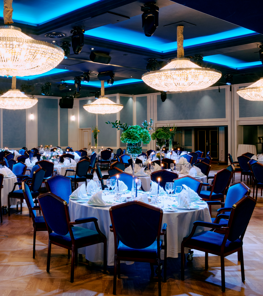 Store, runde bord med hvite duker, to LED-skjermer i bakgrunnen og store lysekroner i taket