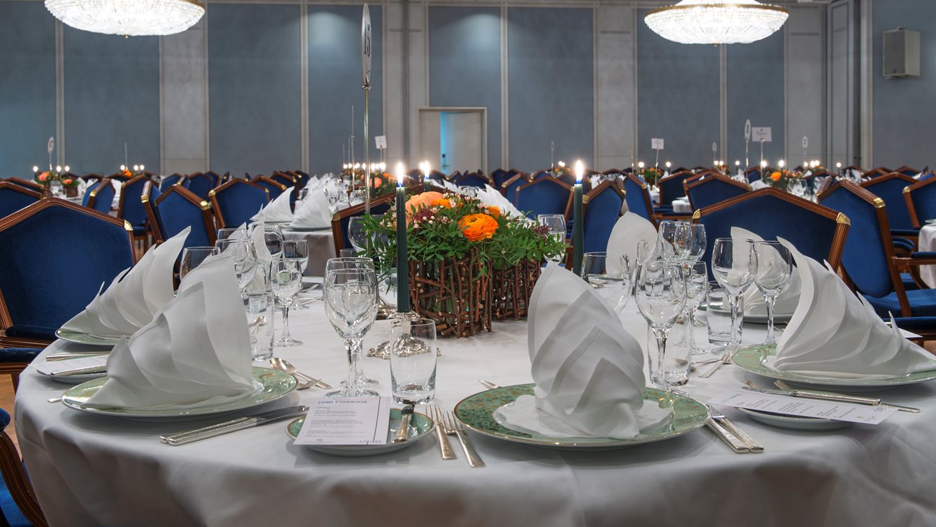 Nærbilde av oppdekket bord i Haakonsalen med brettede servietter og blomster på bordet