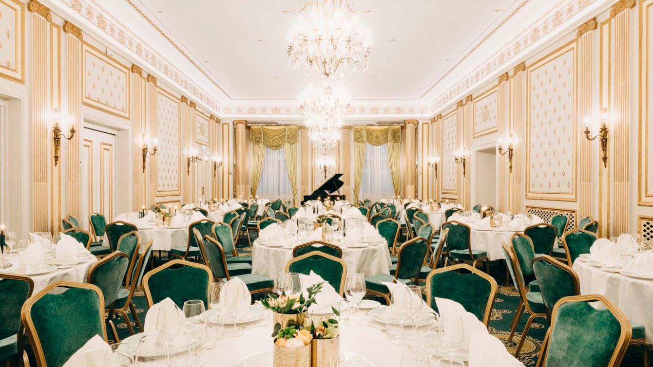 Bright banqueting area with decorated tables, green delicate chairs and chandeliers hanging from the ceiling 