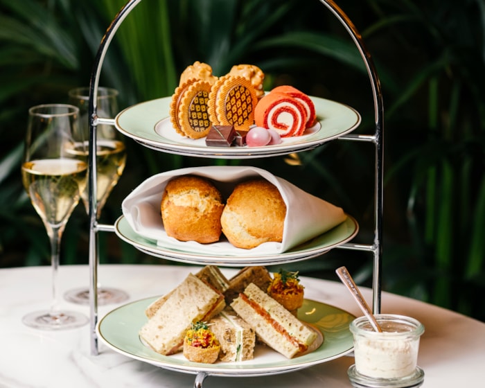 Afternoon Tea servert på tre etasjefat med mini-sandwicher i bunn, scones i midten og kaker på toppen. Ved siden av står to glass Champagne, samt krem og syltetøy i krukker.