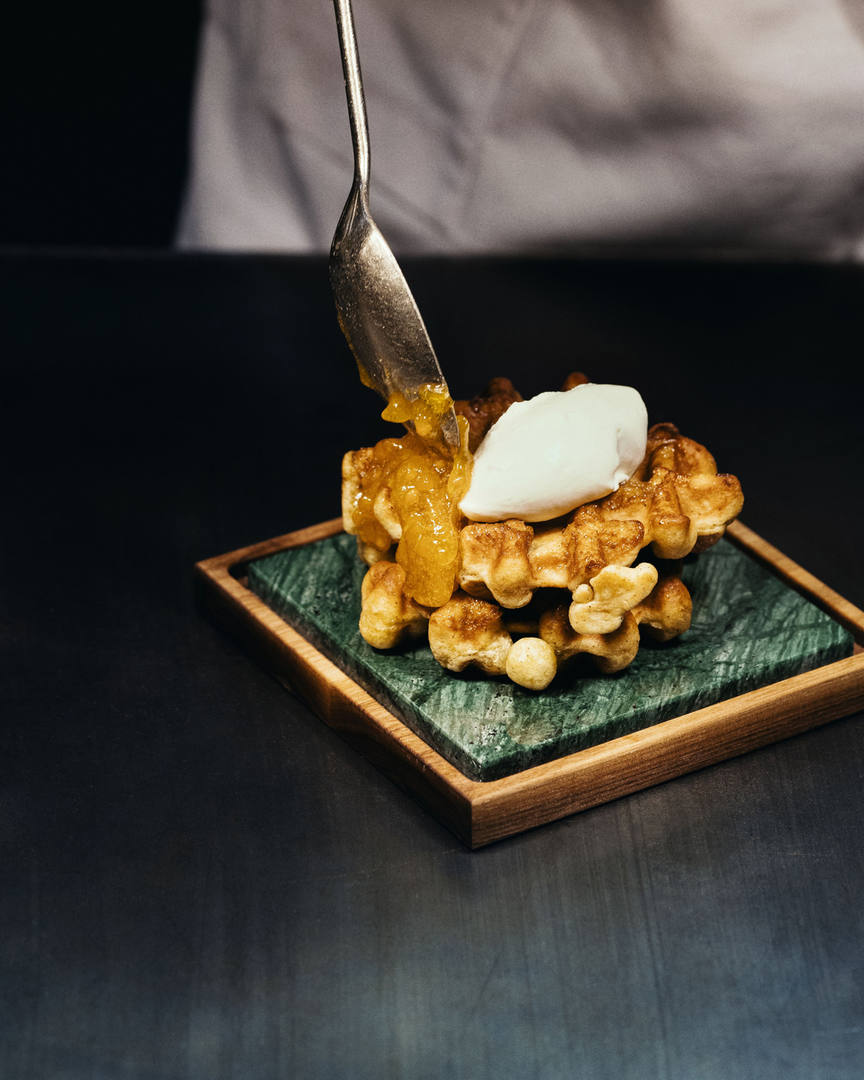 En person holder en skje med syltetøy over belgiske vafler.