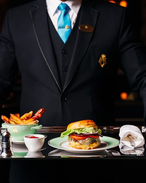 En ansatt holder et brett med hamburger og pommes frites fra roomservice-menyen