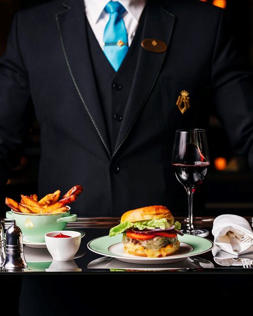 En ansatt holder et brett med hamburger og pommes frites fra roomservice-menyen